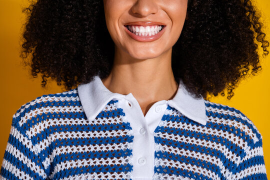 A young woman in a fashionable striped polo shirt smiles confidently with vibrant curly hair and a bright yellow background