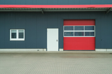 Red garage door and white side door of modern industrial building