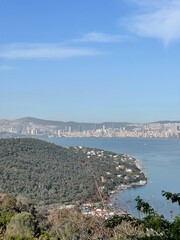 Obraz premium High angle view of the coast with a bay and densely populated urban area visible in the distance, representing a city on the sea and a distant city skyline