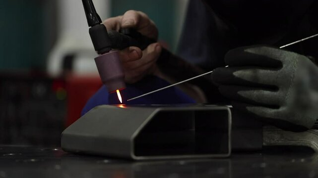 Close up electrode glows red on TIG welder as worker inspects weld