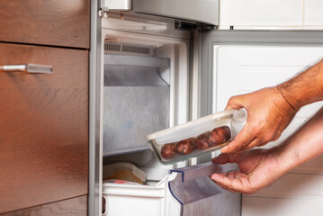 Man's hands putting a food container into the freezer, frozen meals.
