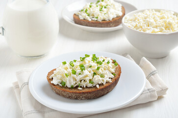 Bread with curd cheese and green onion on white plate