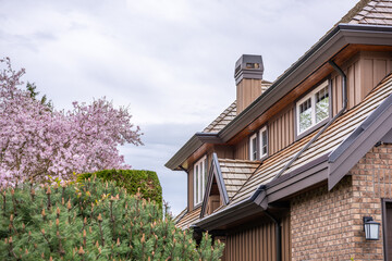 Top of grey stucco luxury house with shingle roof, trees and nice windows in Spring in Vancouver, Canada, North America. Day time on April 2025.