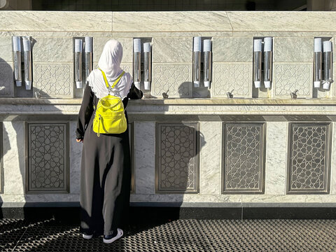 Photo from the back, a beautiful pilgrim girl in a hijab pours holy water zamzam in t