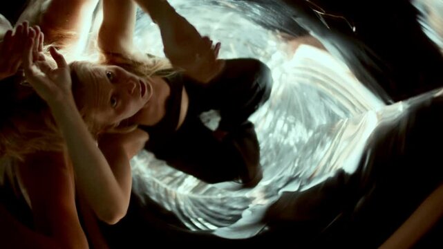 Young expressive woman moving gracefully in distorted mirror reflections and swirling patterns of light. Overhead view