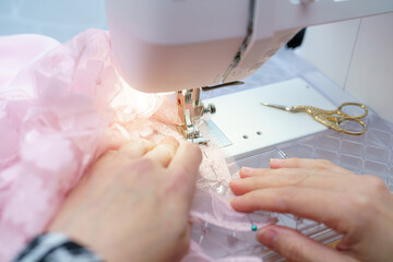 Sewing delicate pink fabric with a sewing machine in a bright indoor workspace during the day