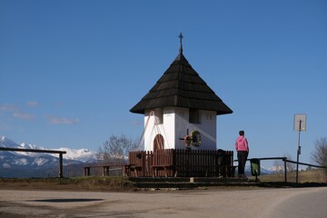 Viewpoint of High Tatras and Bialskie Tatras on Pass over Lapszanka with old white chapel and silhouette of woman in pink jacket.