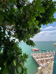 Green foliage framing scenic solarium overlooking Ionian Sea waters, revealing Syracuse's coastal...