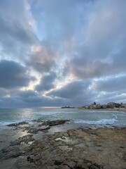 Dramatic sunlight breaking through cloudy skies above rocky coastal landscape in Sicily