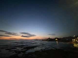 Gentle waves caressing rocky shoreline during vibrant sunset over Santa Croce Camerina, Sicily, illuminating tranquil coastal scenery