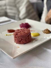 Delicate beef tartare garnished with edible flowers, accompanied by artisan sauces, elegantly plated in historic medieval Gradara restaurant setting