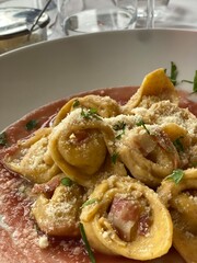 Close-up of tortellini with bacon, parmesan, and herbs in a pink sauce, showcasing Italian cuisine in Gradara, Marches