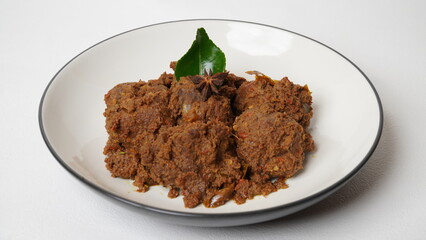 Traditional Indonesian rendang beef dish served on white plate isolated on white background