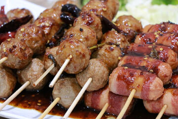 Grilled Meatballs. fish ball and sausage hotdog grilled in stick on tray, Fried pork meatballs skewers bamboo on a white plate with spicy sauce on a table, Thai street food.