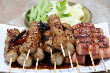 Grilled Meatballs. fish ball and sausage hotdog grilled in stick on tray, Fried pork meatballs skewers bamboo on a white plate with spicy sauce on a table, Thai street food.
