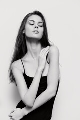 Fototapeta premium Elegant young woman in a black bodycon dress striking a graceful pose against a soft white background, exuding confidence and beauty.