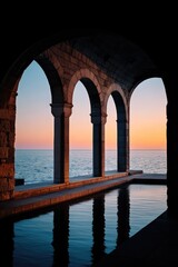 Serene stone arches frame ocean sunset view; reflection in water; vacation stock