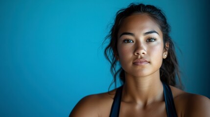 A young woman's determined gaze against a vibrant blue backdrop, showcasing her strength and resilience with soft lighting.