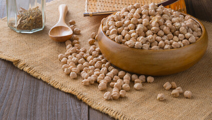 Background with chickpea seeds in wooden bowl and chickpeas lying on burlap cloth on a wooden table