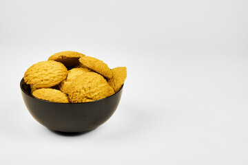 A plate of cookies sits on a white background. The cookies are small and round, and all the same color. The plate is black, and the cookies are arranged in a pyramid shape, one on top of the other.