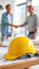 Construction workers shake hands; blueprints and a hard hat on a table