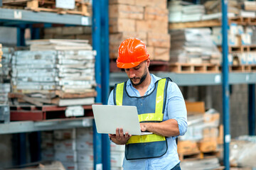 caucasian warehouse worker checking using laptop. caucasian man wearing safety examine storage area with notebook document. supervisor guy wear helmet safety vest at workplace inspect stock by laptop