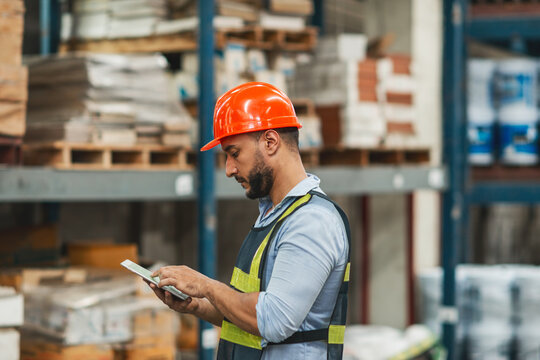 caucasian warehouse worker checking using tablet. caucasian man wearing safety examine storage area with touch screen document. supervisor wear helmet safety vest at workplace inspect stock by tablet