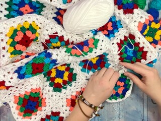 Female hands and crocheting process granny square blanket making with clews of yarn and cozy home photo