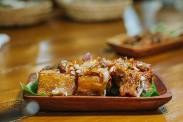 Deep fried crispy pork belly with sambal matah on a wooden plate with bokeh background. Balinese traditional culinary.