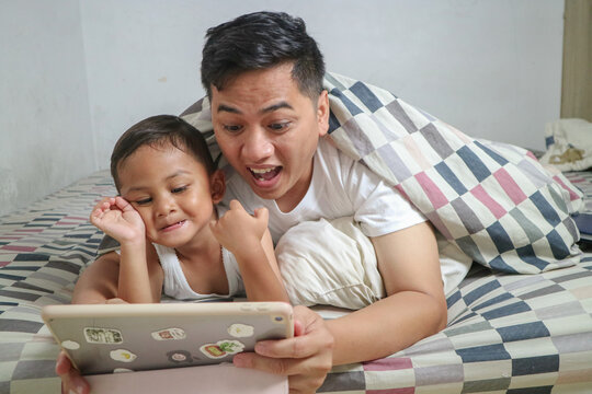 Affectionate father and son using digital tablet in bed at home - Powered by Adobe