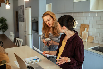 Lesbian couple reading bills with laptop in modern kitchen