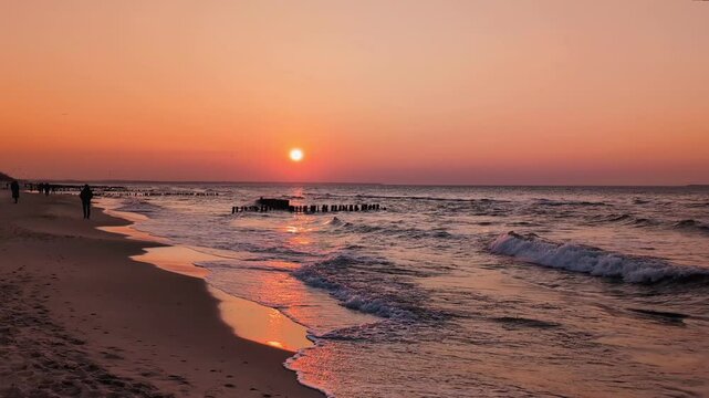Bright sunrise or sunset on the beach, shining waves over the sea, calm ocean, pink sky walking people, warm golden sun on the horizon, bright evening landscape, natural environment near the city