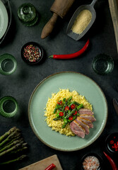 Roasted duck breast with asparagus, chili and couscous featuring kitchen utensils surrounding plate