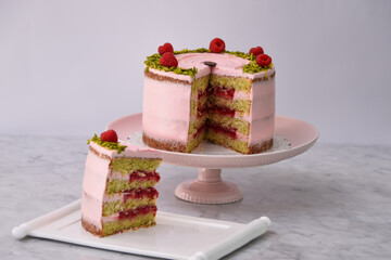 Elegant Raspberry Pistachio Layer Cake with Slice frosted with light pink cream and garnished with...