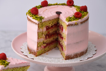 layered Raspberry Pistachio Cake round frosted with light pink cream and garnished with fresh raspberries and chopped pistachios closeup side view of baked delicious dessert