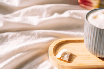 Two pouches of snus next to morning coffee with foam on white bed linen, dawn.