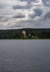 Rättviks Kyrka is visible on the shore of Siljan lake, surrounded by lush greenery, as dark storm clouds loom overhead on a rainy summer day in Dalarna, Sweden.
