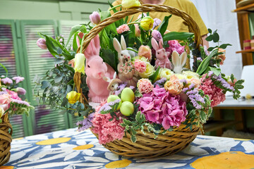Close-up of a male florist in a yellow T-shirt holding a large Easter basket with pink flowers and...
