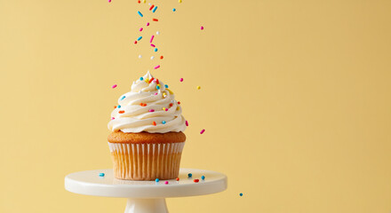 Frosted cupcake on pedestal with sprinkles falling in studio light