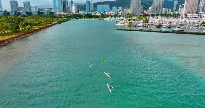 A few sportsman practicing kayaking. People on canoe row along the green waterfront and yacht club. Waikiki scenery at backdrop.