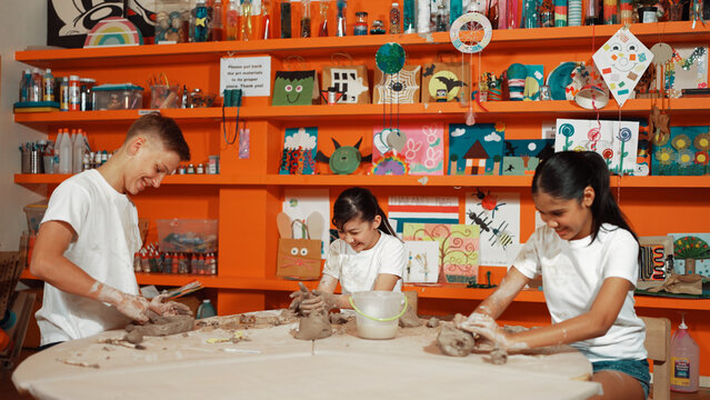 Diverse highschool people working on dough while asian girl modeling clay at pottery workshop. Group of happy diverse children working or making cup of clay. Creative activity concept. Edification.