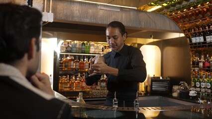 Asian smart bartender shaking mixed cocktail preparing to serve at luxurious counter preparation making special drink serving to customer fronted bar. Special refresh drink nightlife luxury. Vinosity.