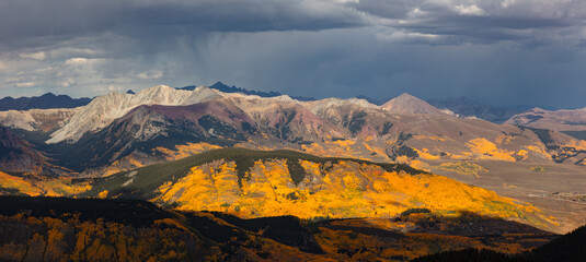 High in the mountains, warm light accents the Elk Range peaks covered in colorful aspen trees on a...