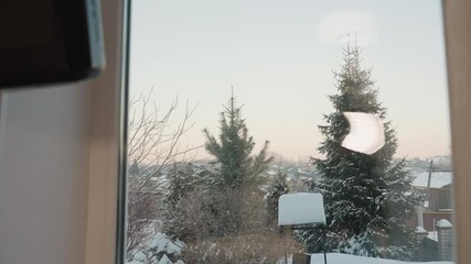 Outdoor view of snowy environment featuring pine trees and snow-covered bushes with a well in the compound, rooftops of distant homes, and soft pastel sky during cold winter morning - Powered by Adobe