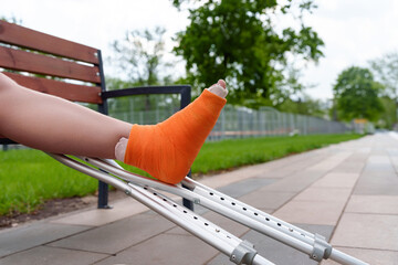 Close-up of cast-encased leg in orange bandage resting on metal crutch, conveying mobility...