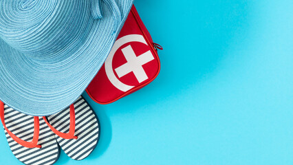 Summer sea vacation. Top view of red first aid kit indicating safety and preparedness during sea voyage and also hat, flip flops on blue background.
