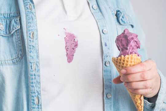 A person spilled purple ice cream onto their white shirt while enjoying a treat in a light blue denim jacket. The playful mishap adds humor to a casual moment.