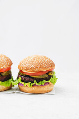 Vegetarian Burger made with vegan cutlet, burger bun, salad, cucumber, cheddar cheese and onion on a light concrete background. Delicious vegan food