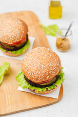 Vegetarian Burger made with vegan cutlet, burger bun, salad, cucumber, cheddar cheese and onion on a light concrete background. Delicious vegan food
