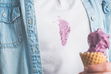Close up spilled purple ice cream onto their white shirt while enjoying a treat in a light blue...